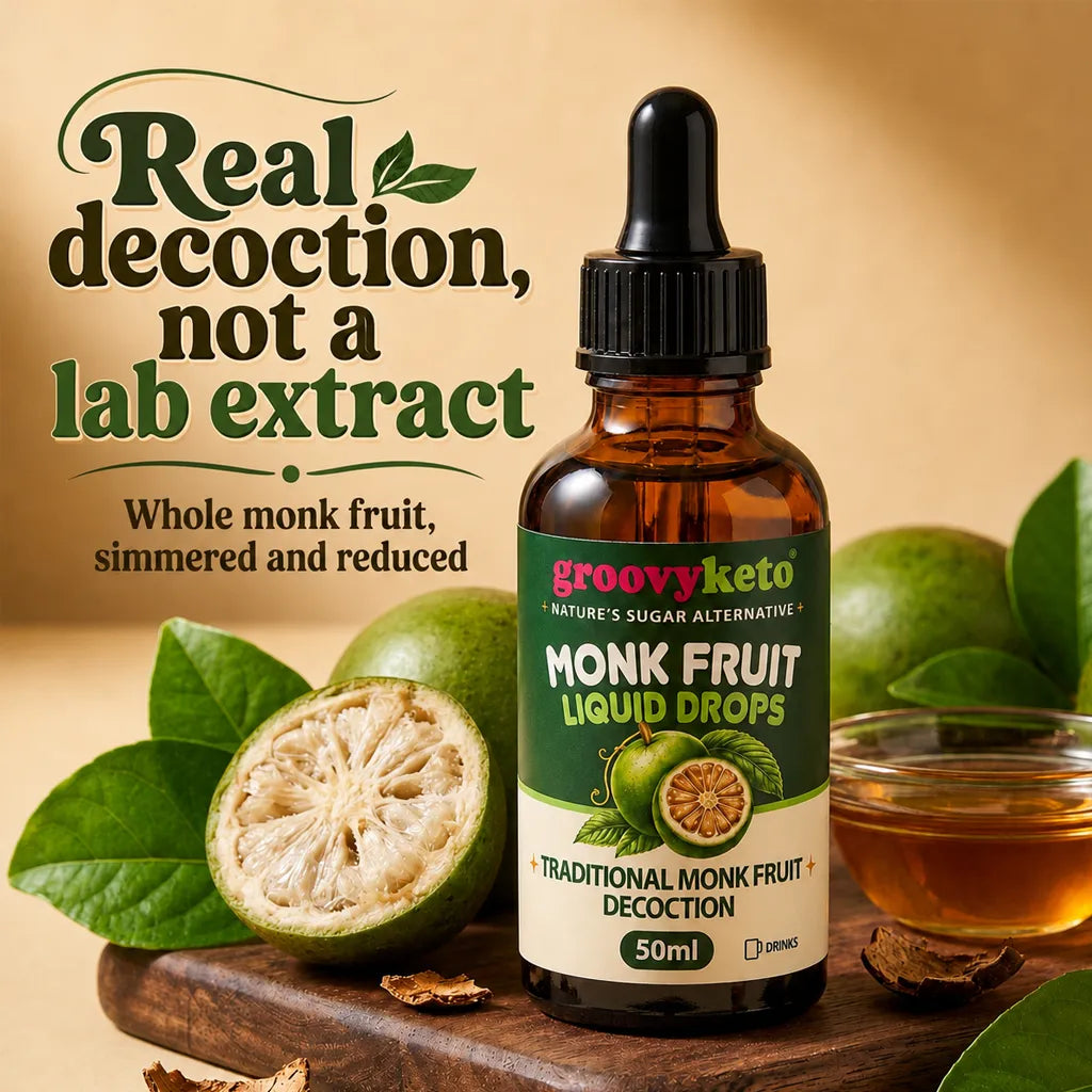 A bottle of groovyketo Monk Fruit Liquid Drops centered on a wooden surface, surrounded by whole and sliced monk fruit, green leaves, a small bowl of amber liquid, and promotional text reading 'Real decoction, not a lab extract.' The product itself is an amber glass dropper bottle with a black cap and a green-and-white label.