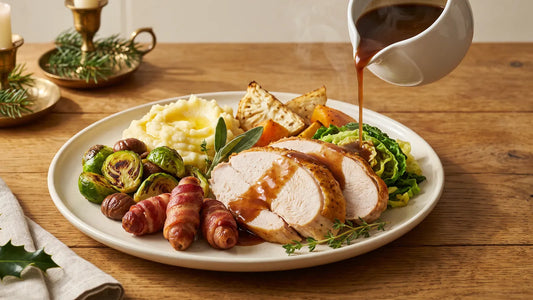 Keto Christmas dinner plate of sliced roast turkey, pigs in blankets, roasted Brussels sprouts and chestnuts, cauliflower mash, roast celeriac and swede and savoy cabbage, with gravy poured from a white jug
