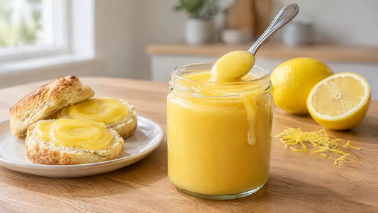 Keto lemon curd in a glass jar with a spoon, beside split scones spread with lemon curd and fresh lemons